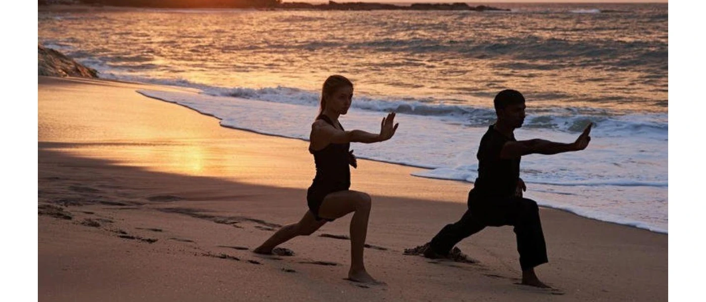 Two figures at sunset on the sand practicing yoga as waves wash ashore
