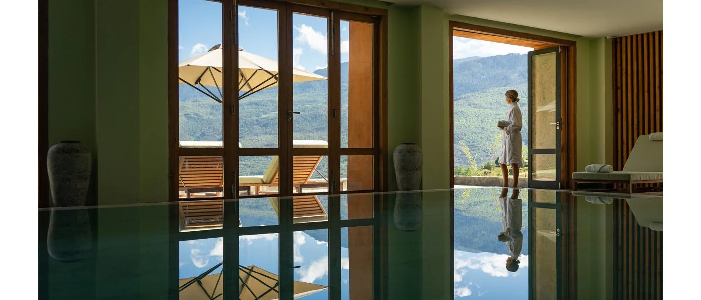 Robed woman looking at a view of green hills, standing next to an indoor pool