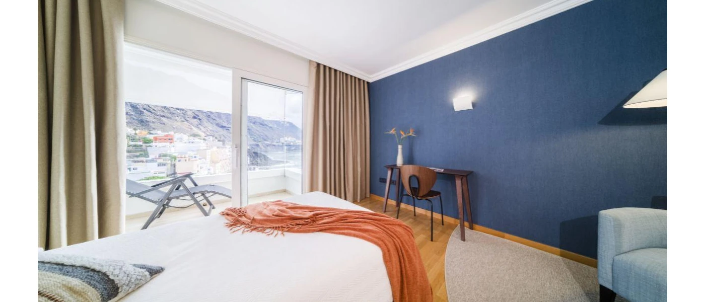 Dark blue wall, neutral curtains and white bedding and a terracotta throw