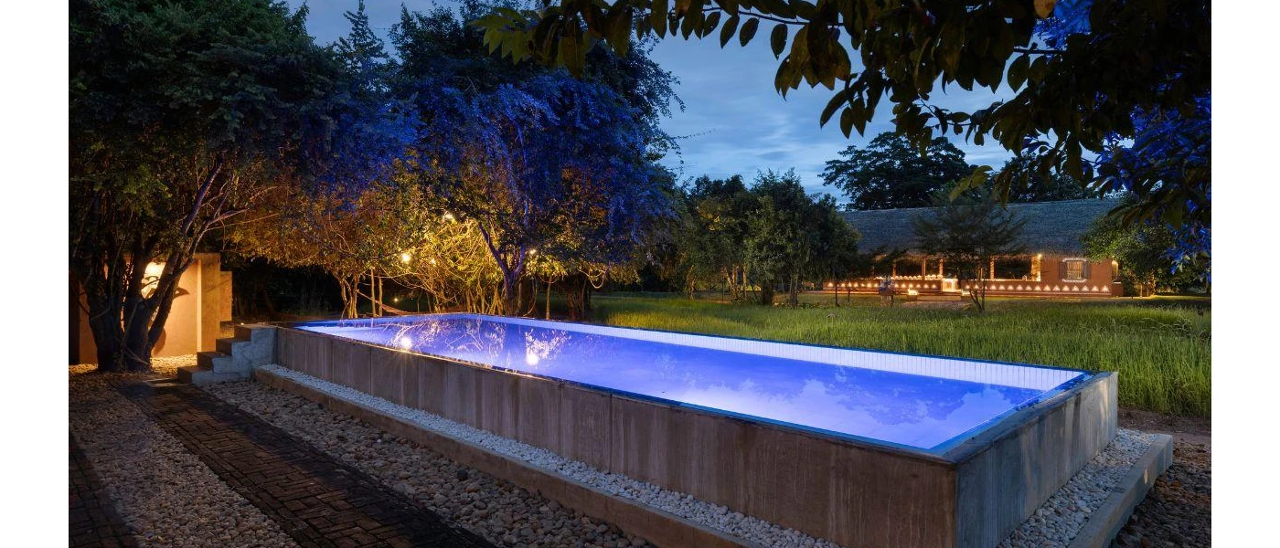 Rectangular swimming pool lit by surrounding lights as the sky darkens 