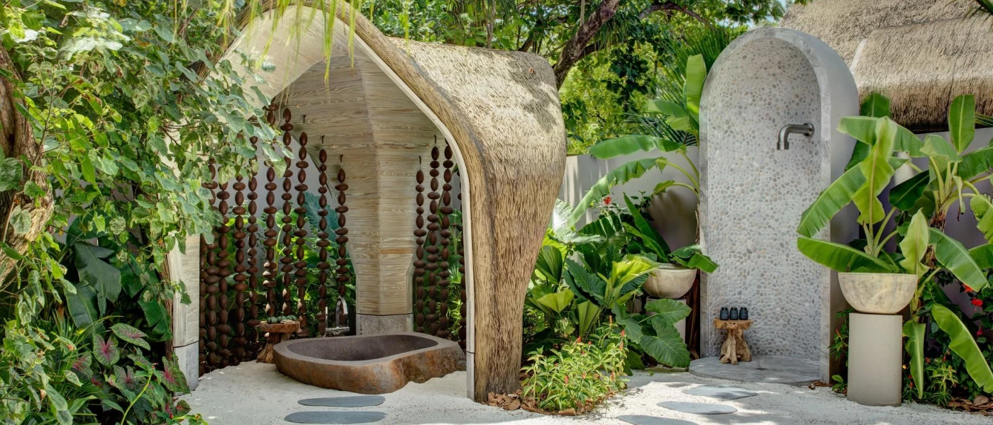 Cobbled stone courtyard with thatched-roof cubbyholes, with an outdoor shower and bathing area fringed with tropical greenery