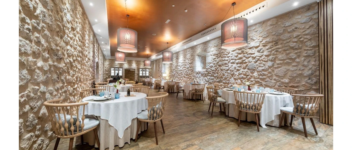 Restaurant with large-stone walls, tables with white tablecloths and wooden chairs laid out for meals