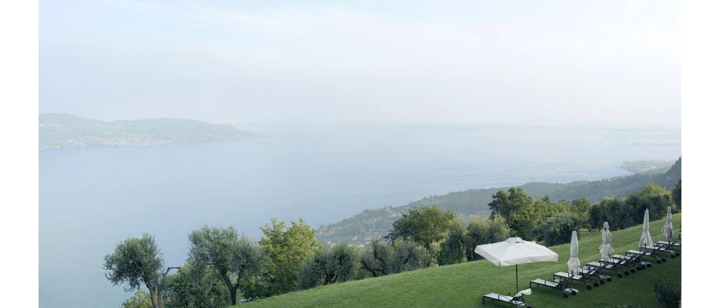 White loungers and umbrellas on a grassy lawn overlooking a misty lake