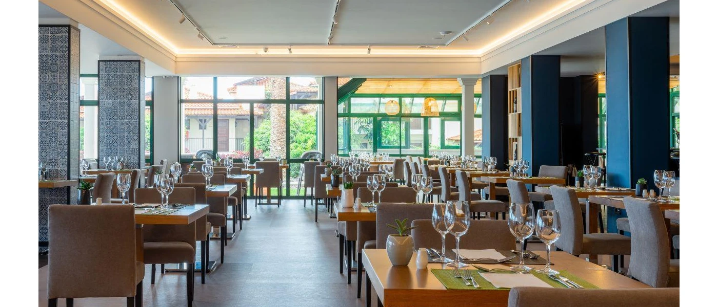 Large restaurant with full-length windows, rattan lantern-style lighting, and neutral tables laid up for diners
