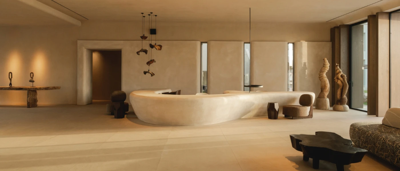 Ultra-modern room with limewashed cream walls, a cream marble-look desk area, wooden sculptures and furniture and a cluster of hanging pendant lights in a brass hue