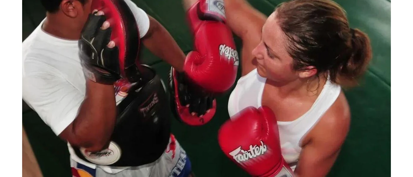Woman in a white vest and boxing gloves spars with a trainer wearing pads
