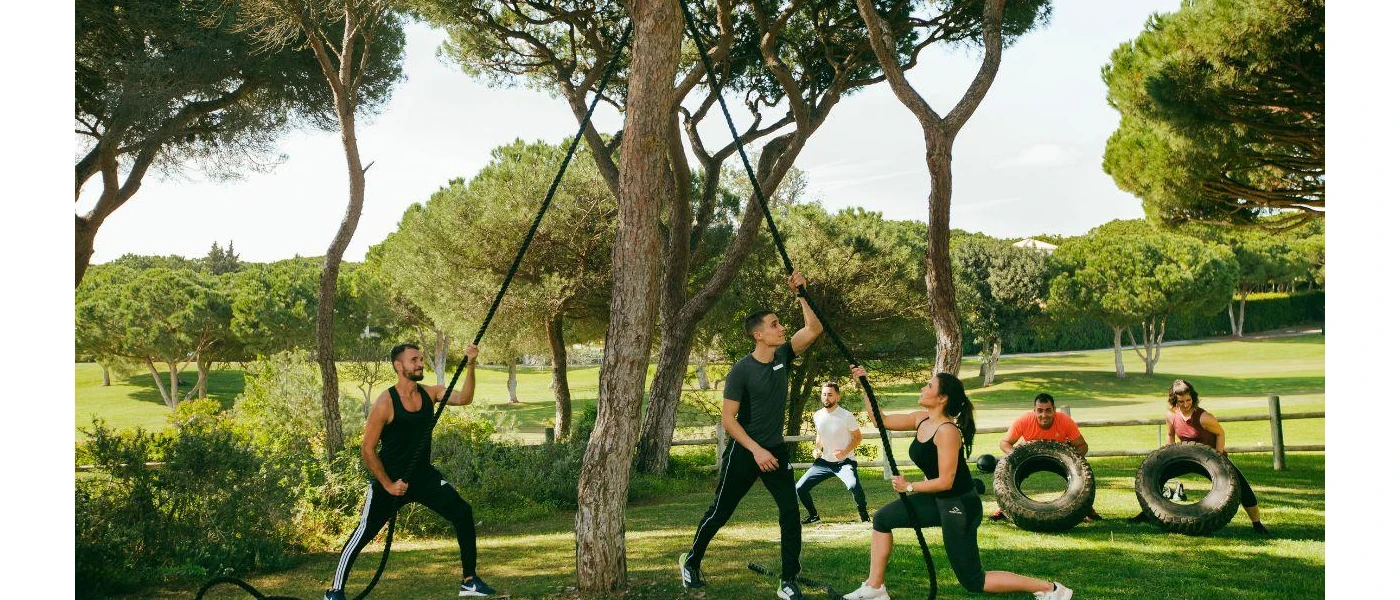 Group during a fitness class using ropes, tyres and weights - taking place in a leafy garden