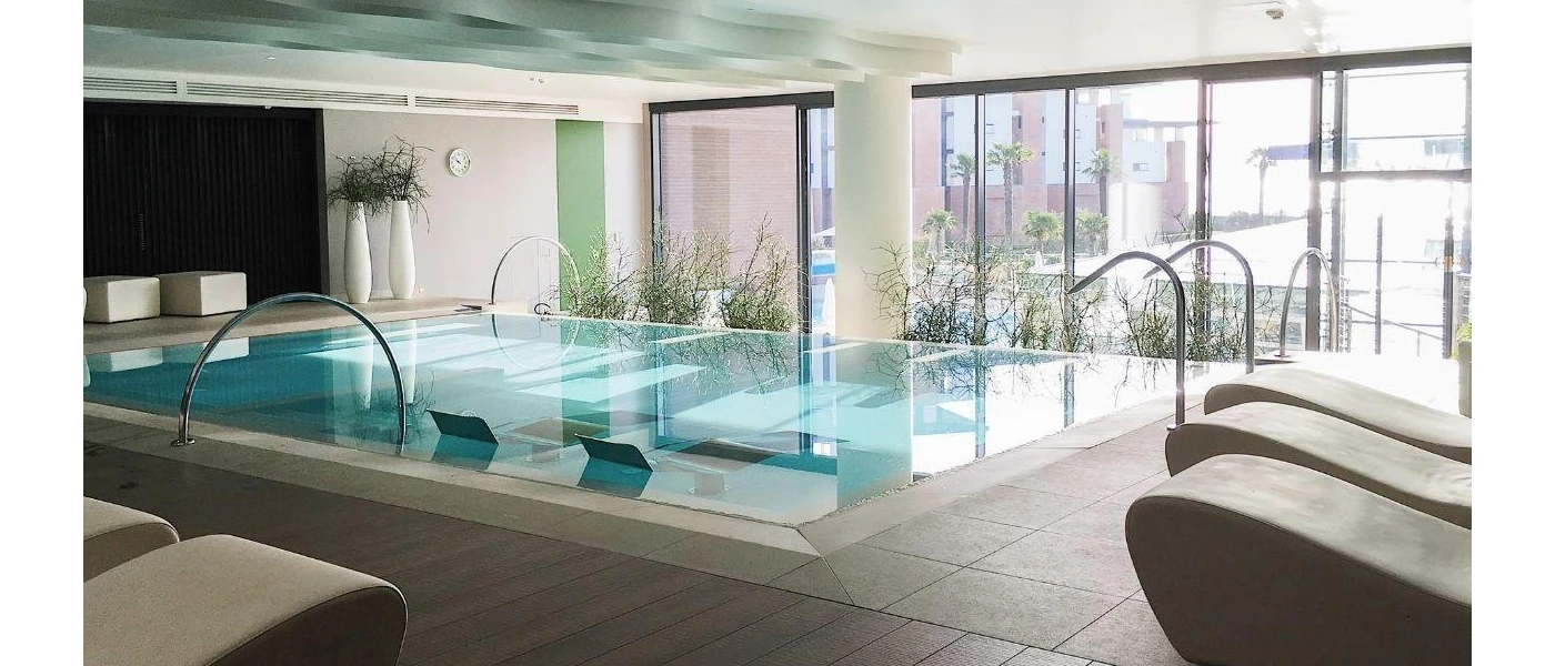 Sleek indoor pool surrounded by cubist crea, loungers and floor-to-ceiling windows