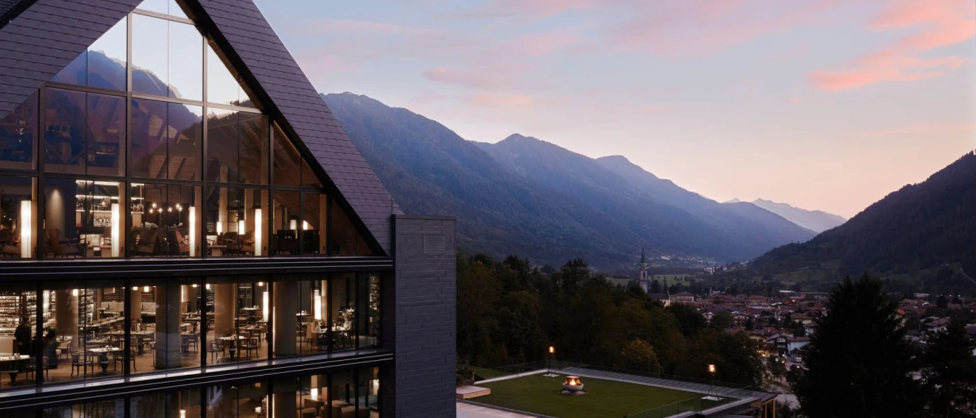 Exterior of Lefay Resort & Spa Dolomiti, angular building with full-length windows overlooking mountain peaks and a twinkling village below