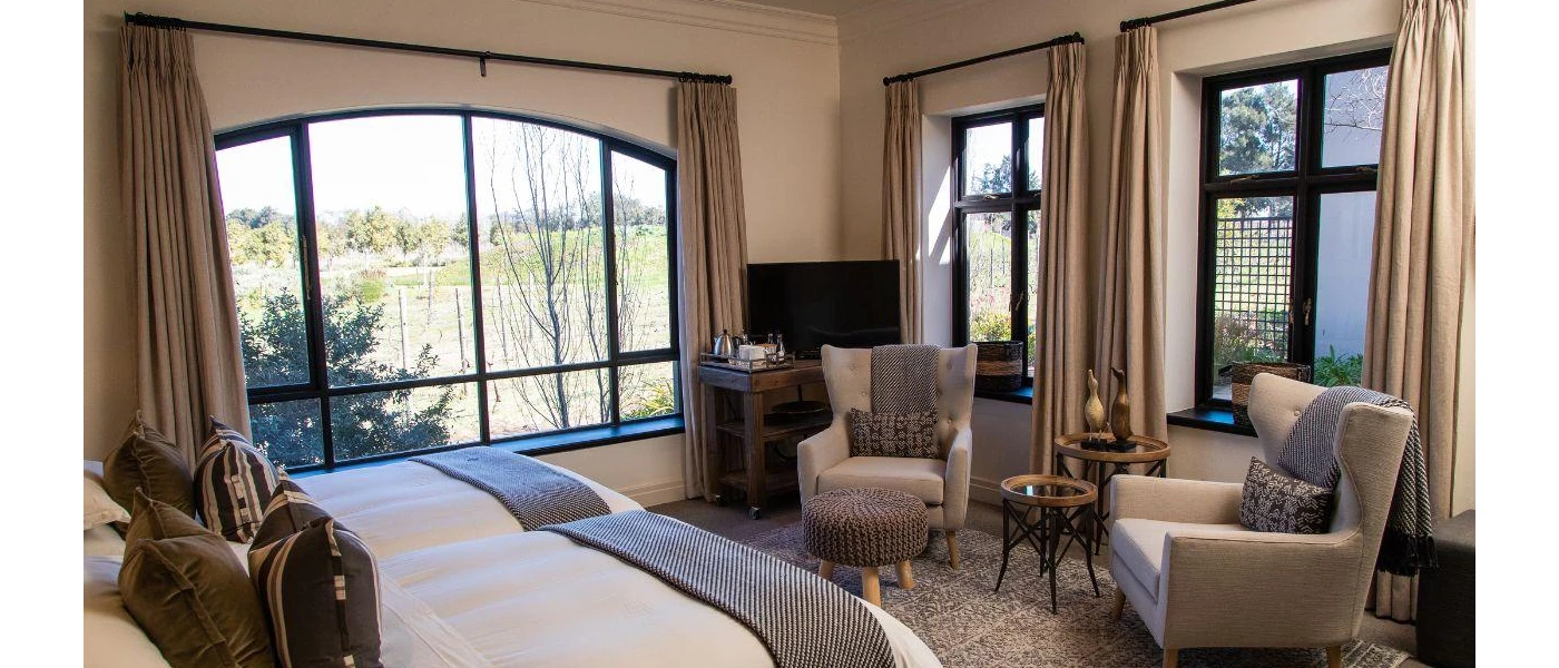 Neutral hotel room bedroom with biscuit-coloured walls, beige curtains, white bedding and patterned cushions in brown and beige