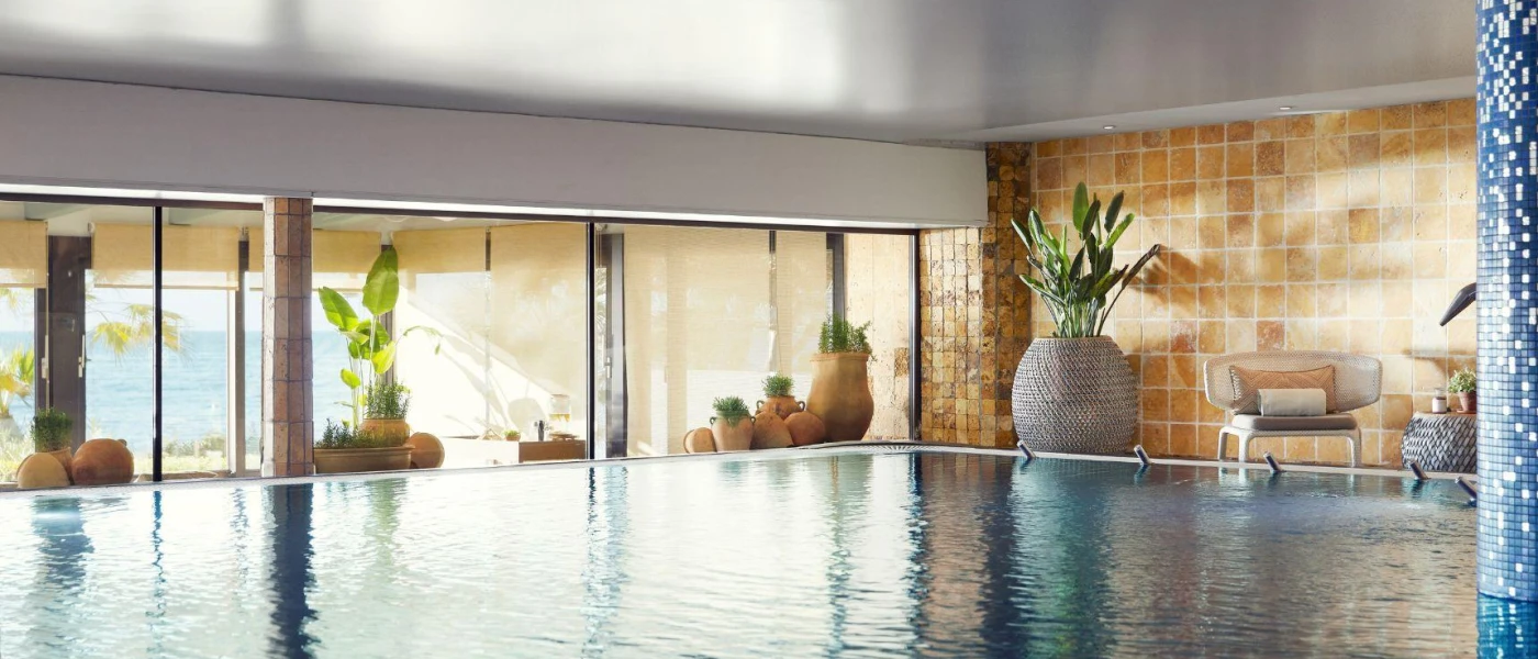 Large indoor pool surrounded by terracotta plant pots, floor-to-ceiling windows and blue tiled columns