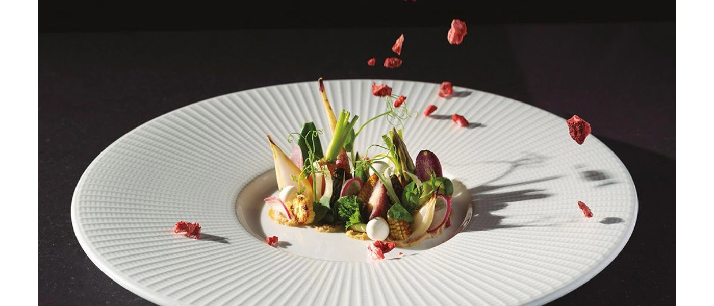 White plate with a vegetable salad with pomegranates being tossed on top 