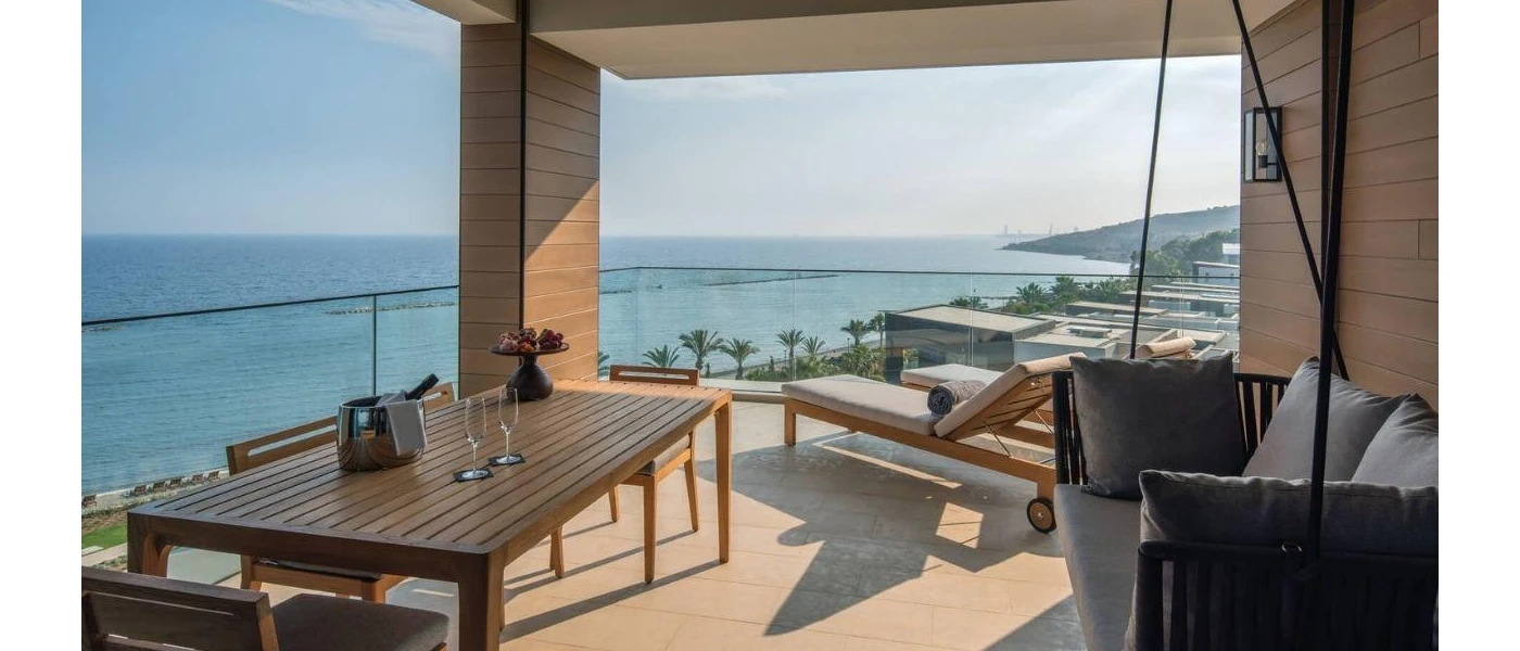 Large oceanfront balcony with a wooden dining table, cushioned hanging seat and loungers
