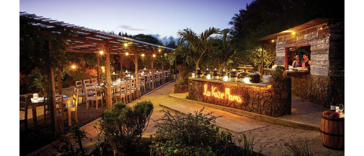 Rustic open-air restaurant with wooden pagoda, tables and chairs, and a lit up sign reading 'La Kaze Mama'