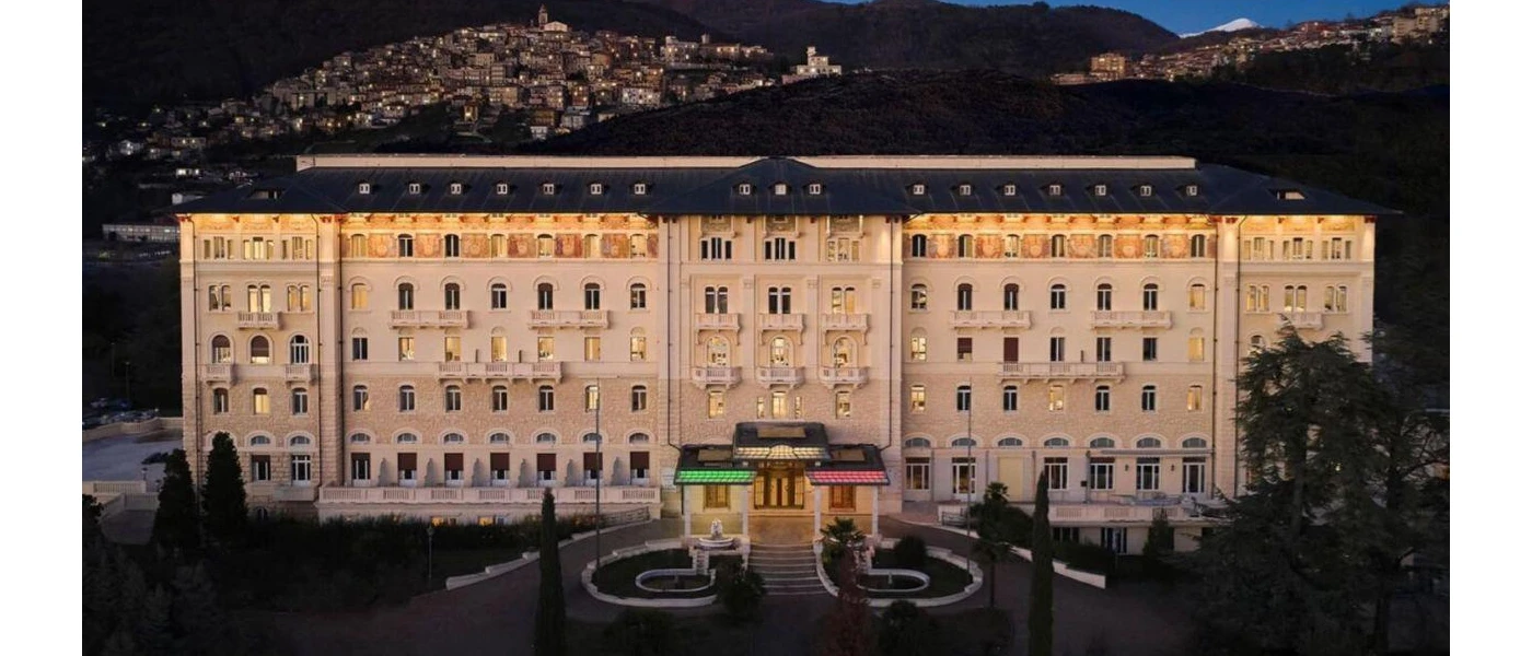 Palazzo Fiuggi's exterior, showing multiple storeys and light sand coloured walls surrounded by greenery