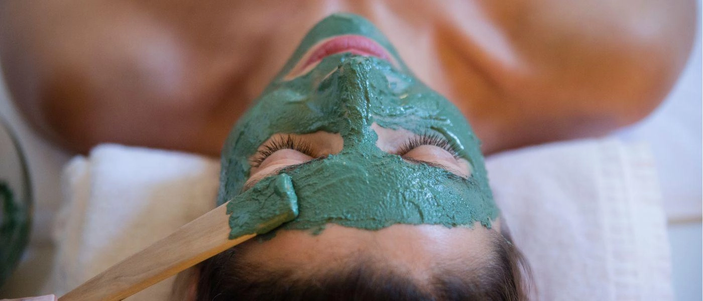 A lady with green mud on her face having a facial done