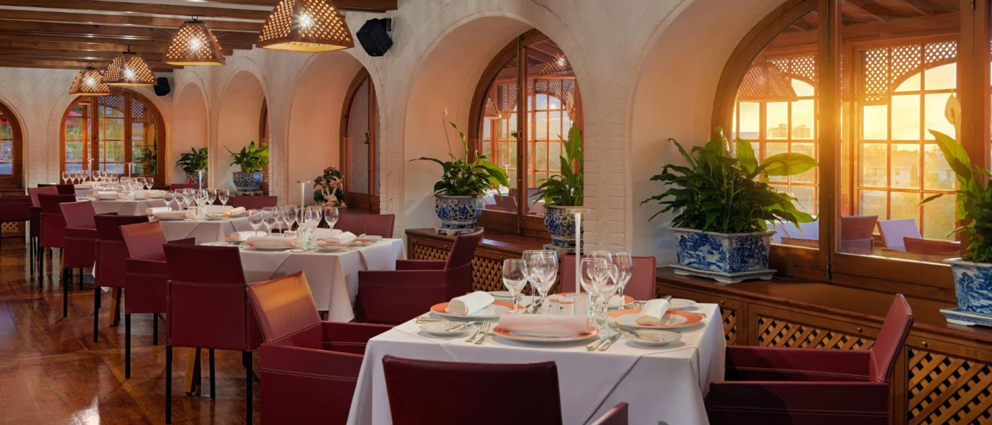 Colonial-style restaurant with cream walls and wooden ceiling beams, swooping archways, plants in blue and white china pots and crisp white tablecloths