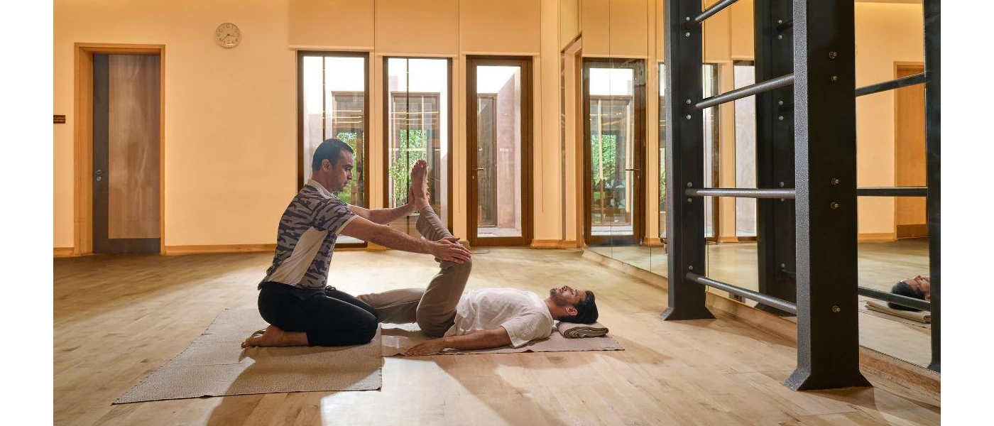 Man lies on his back in an airy studio as a staff member lifts one leg up in the air