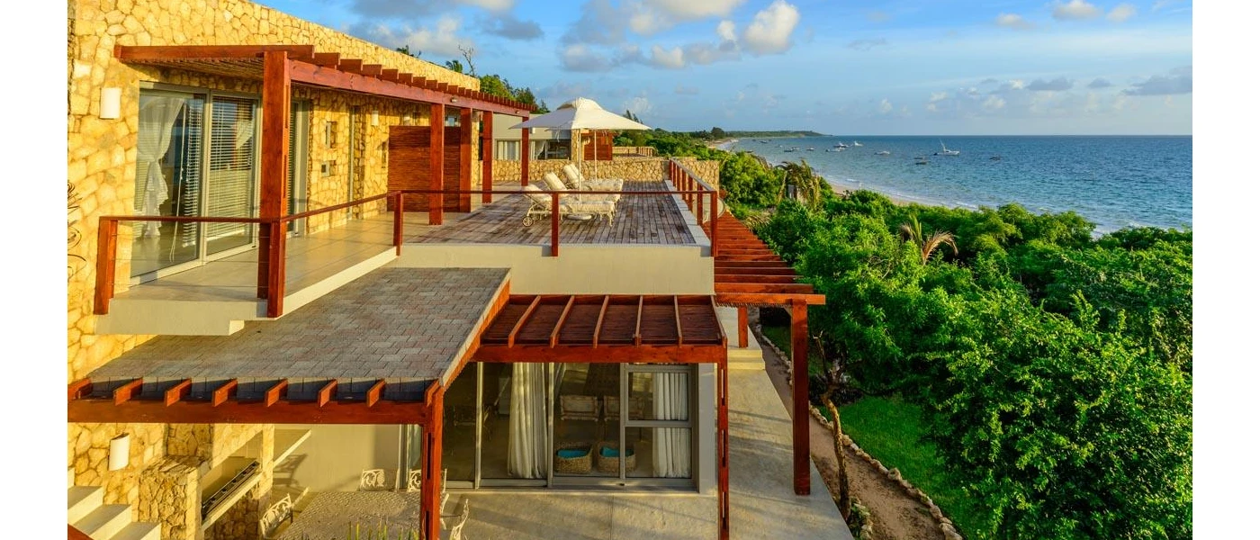 Stone building with glass-fronted balcony overlooking tropical greenery and the ocean