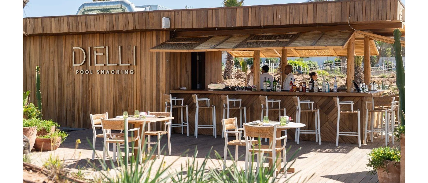 Wood-panelled building with the words Dielli Pool Snacking written on the side and tables and chairs outside