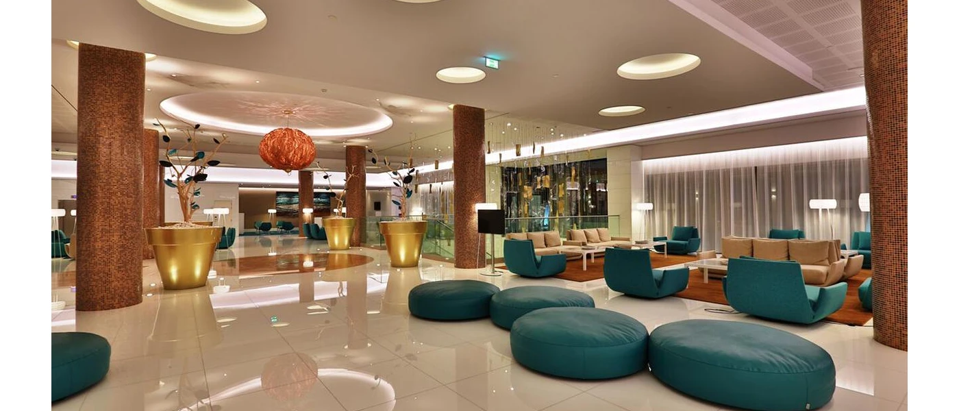 Modern reception with a glossy tiled floor, oversized gold plant pots and a hanging orange ceiling light, teal bean bags and sofas