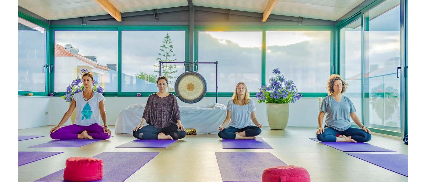 Group of woman on their knees on yoga mats with eyes closed and a sound gong behind them