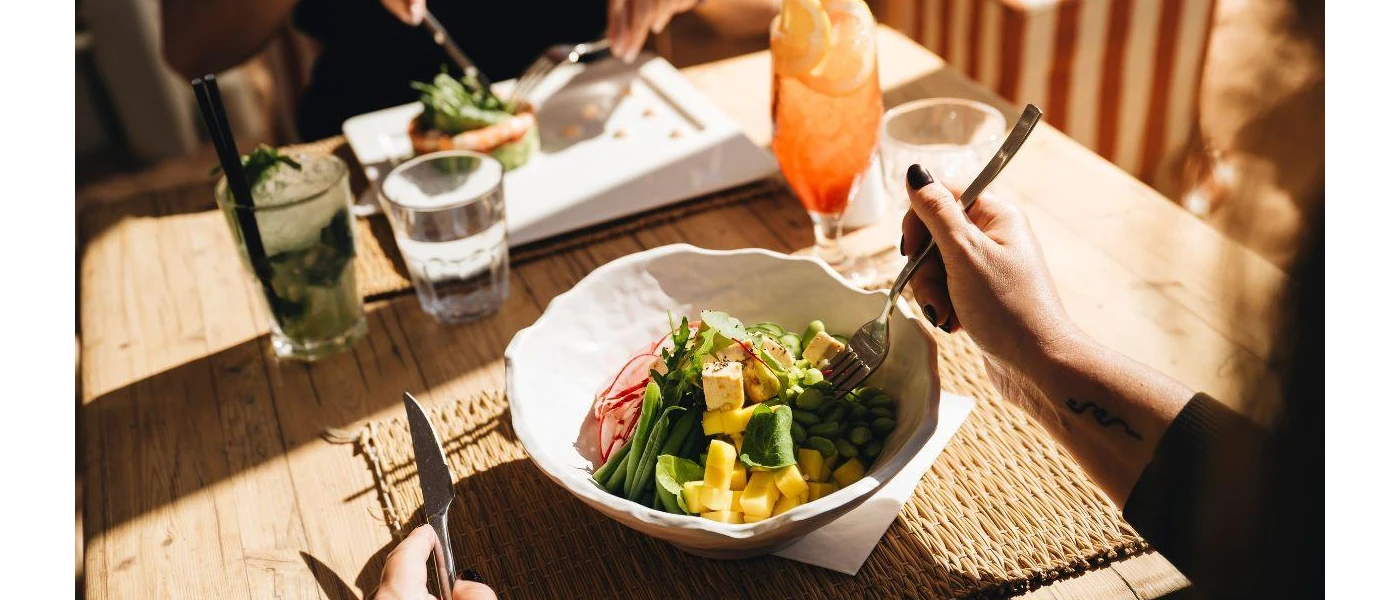 Two people sat down to eat at a table, one with vegetables in a bowl and an orange coloured drink beside her