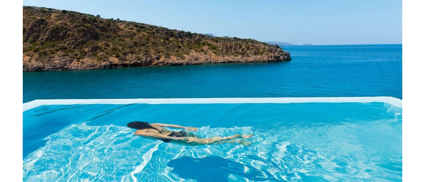 Woman swims underwater in a swimming pool overlooking the sea and a green hillside