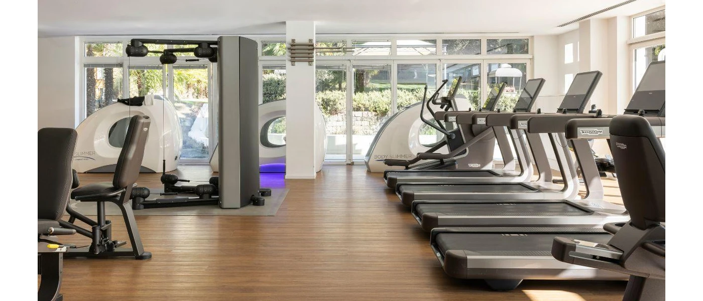 Gym with white walls, wooden floors and ceiling spotlights, with treadmills, weight machines and other equipment 