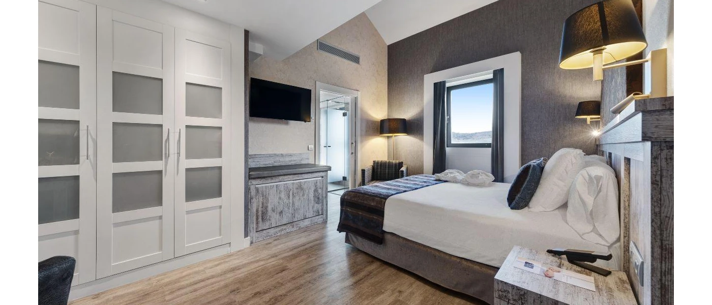 Hotel room with a wooden floor and grey walls, with crisp white bedding, a grey throw and black wall lights