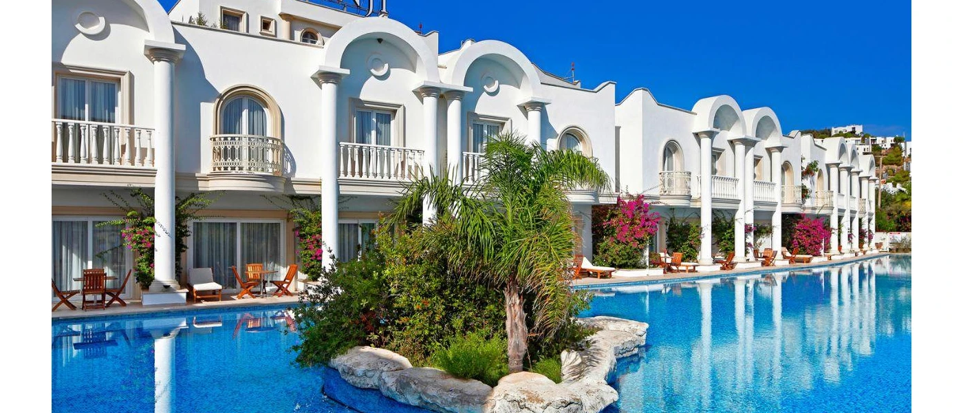 Two-storey white buildings with curved designs, overlooking a swimming pool with a palm island at the centre