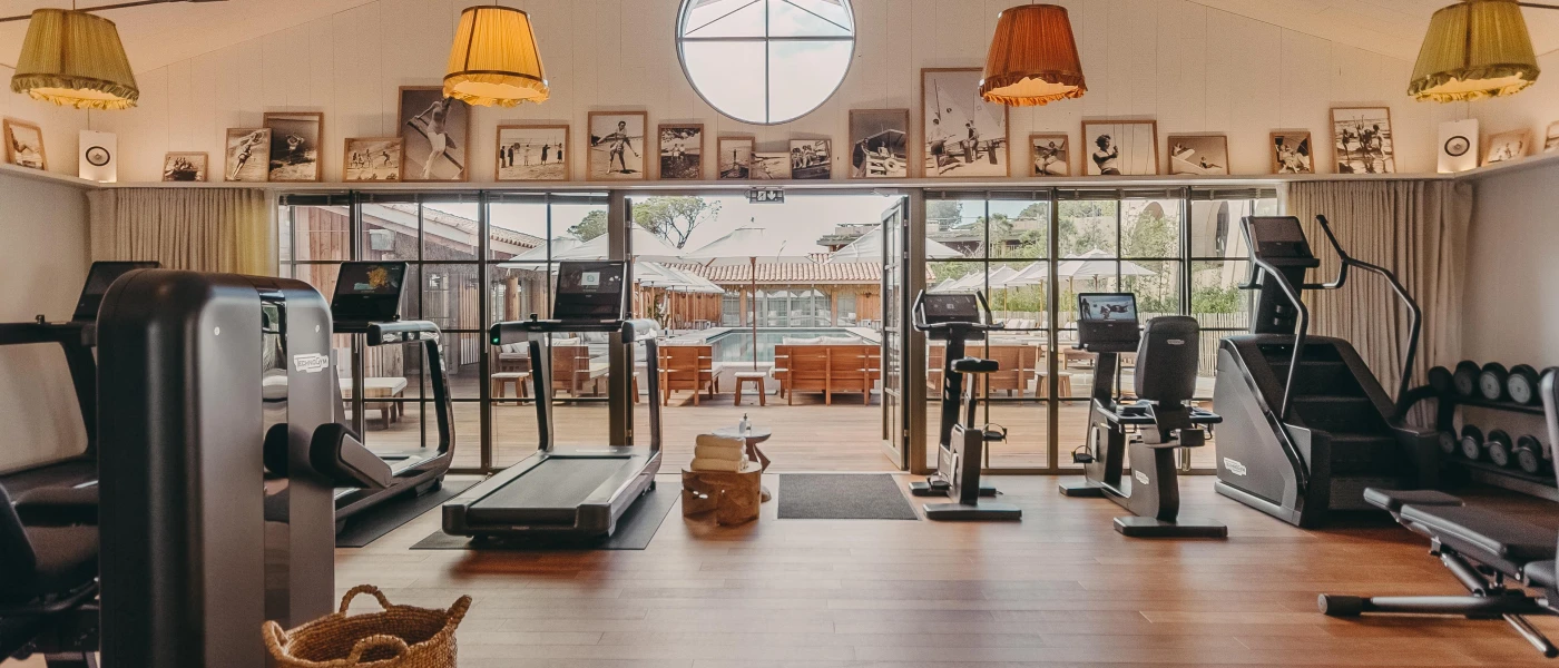 Gym with windows overlooking the pool, treadmills and bikes, quirky fringed ceiling lights and a shelf packed with retro prints