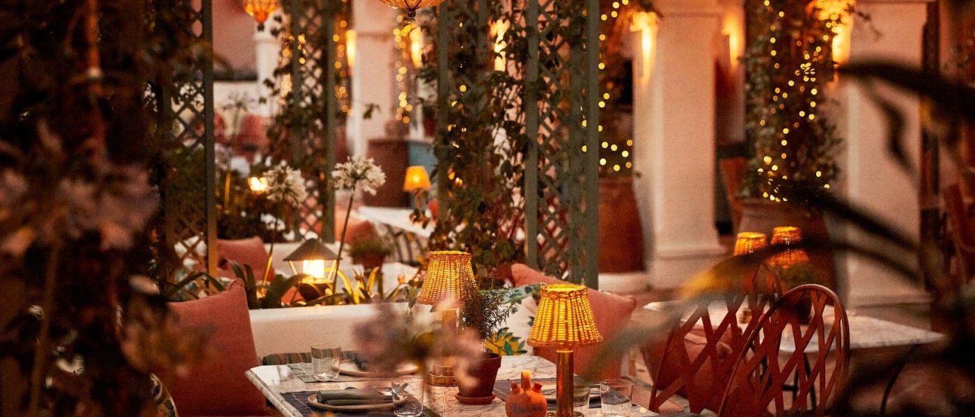 Restaurant with fairy lights, terracotta cushions and table lanterns, plus climbing greenery