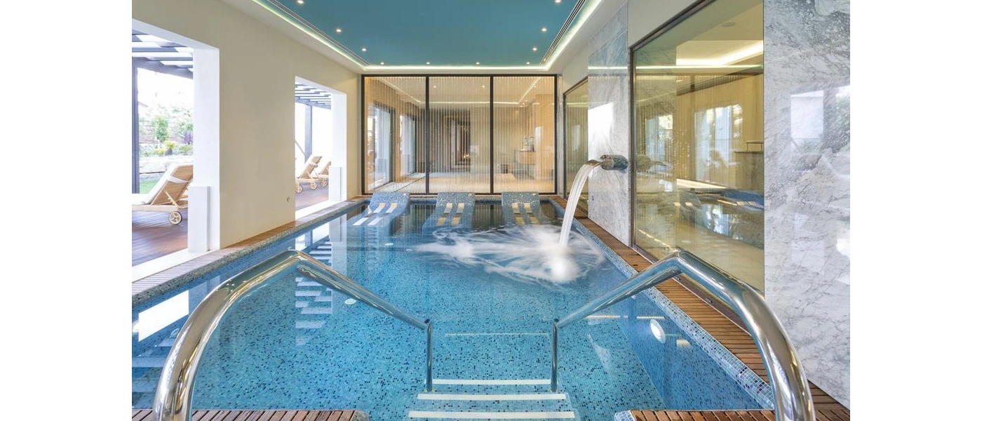 Spa area with a rectangular pool with jets, terrace with white loungers, floor-to-ceiling windows and spotlights