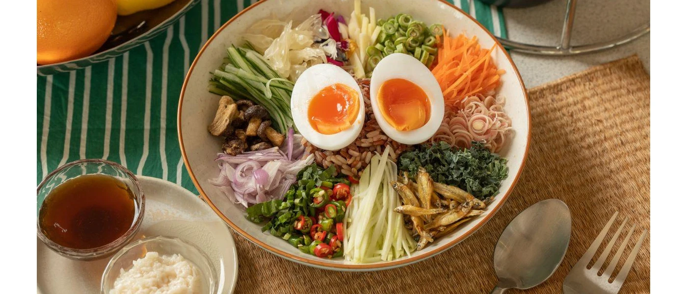 Bowl of healthy food, including an egg, spring onion, rice, carrot, mushrooms, cucumber and sardines
