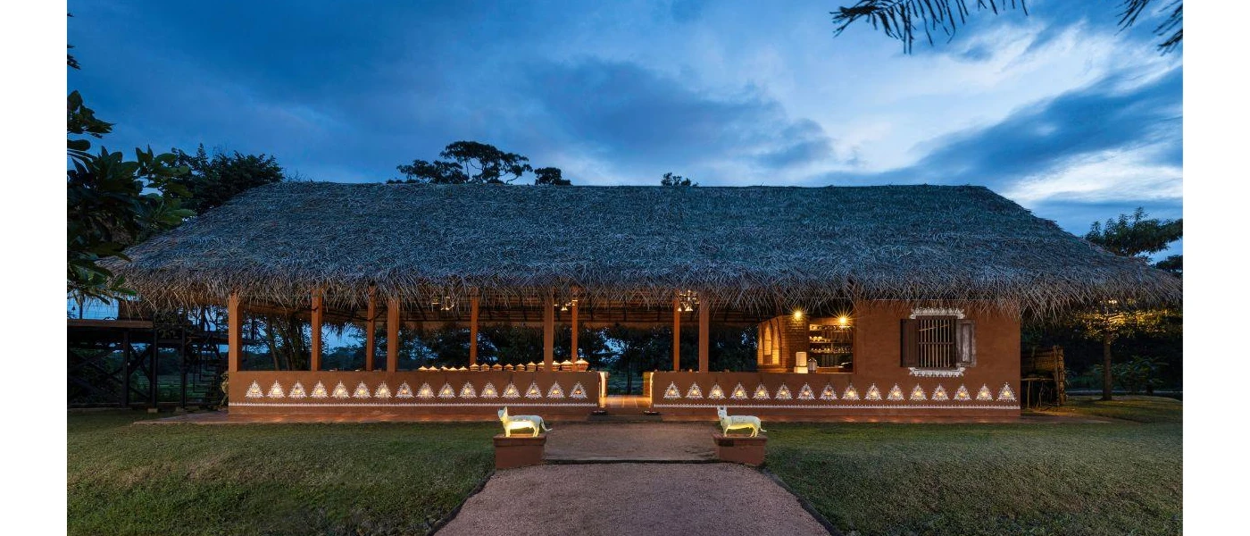 Low-rise thatched-roof pavilion with open sides and animal statues outside, at the bottom of a gravel path