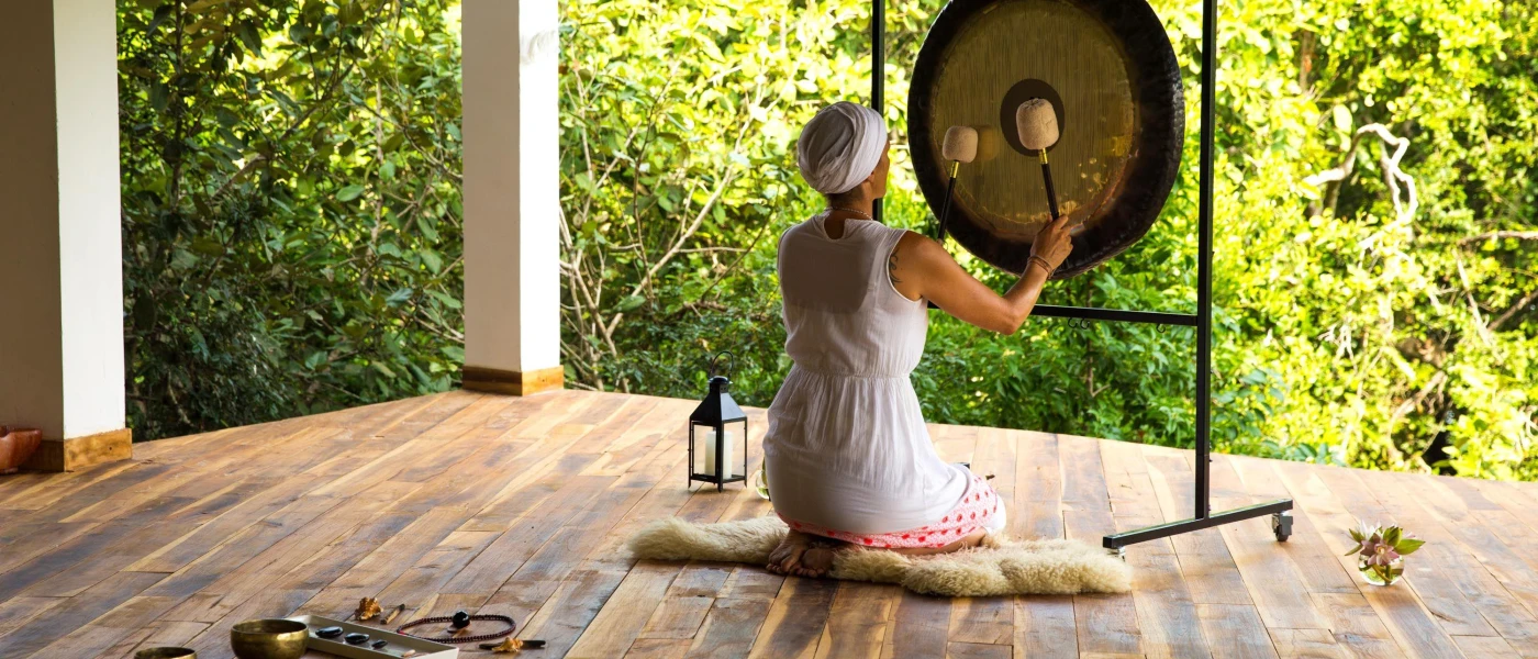 Woman in a white dress and headscarf playing a gong, sitting in an open-air pavilion
