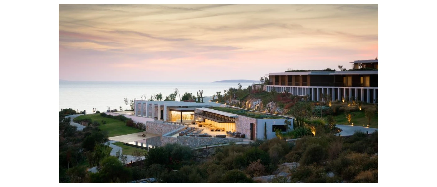 White buildings with clean lines, cobblestone walls, surrounding greenery and the Aegean Sea in the background