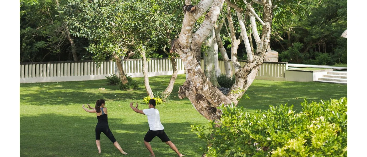 Two people in active wear doing Tai Chi in a tropical garden setting