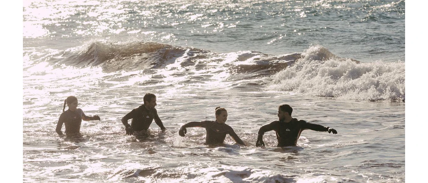 Two men and two women in wetsuits clamber out of the sea in the sunshine