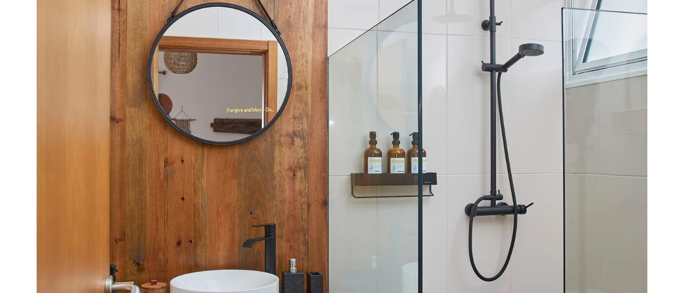 Wooden bathroom with white sink, black hanging mirror and shower with black bottles
