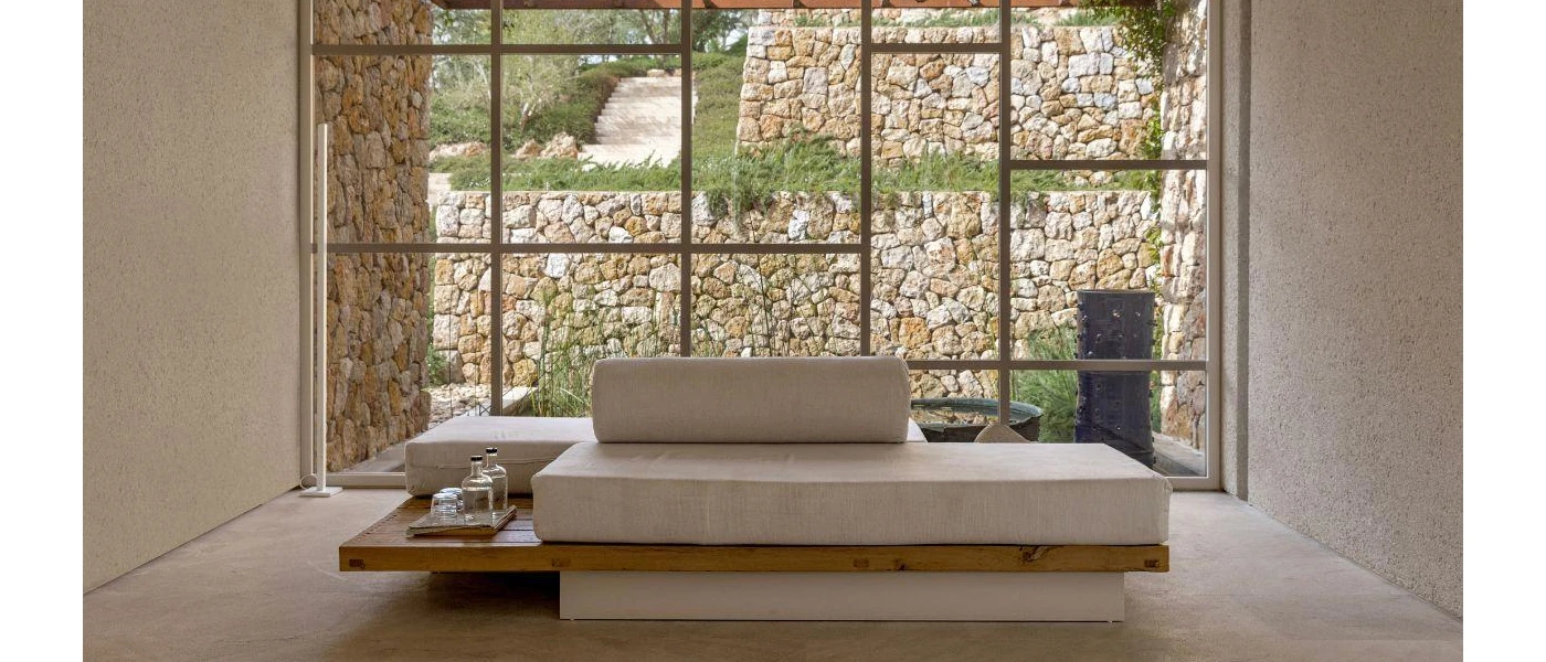 Modern beige sofa with rectangular cushions in front of a floor-to-ceiling window overlooking nature