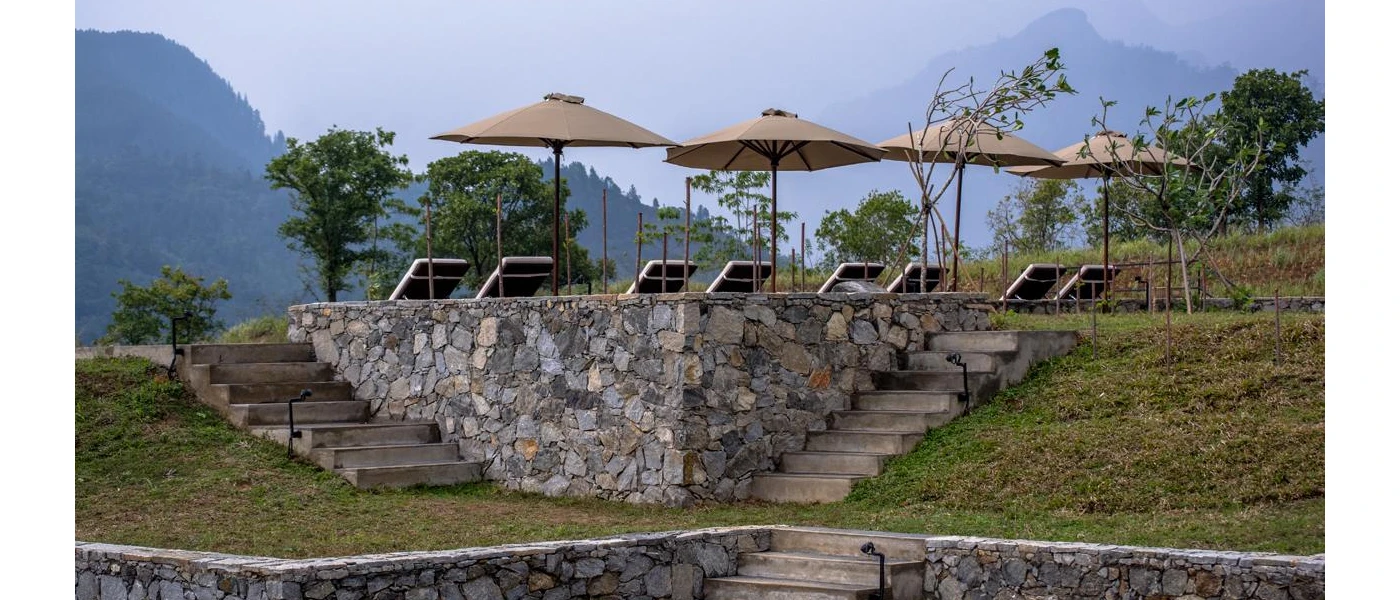 Cobbled stone walls and grassy hills next to a terrace of loungers and parasols and a mountain view