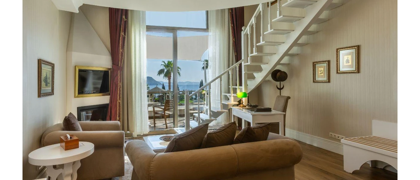 Living area with camel-coloured seating, a desk, TV and gold framed pictures on the wall