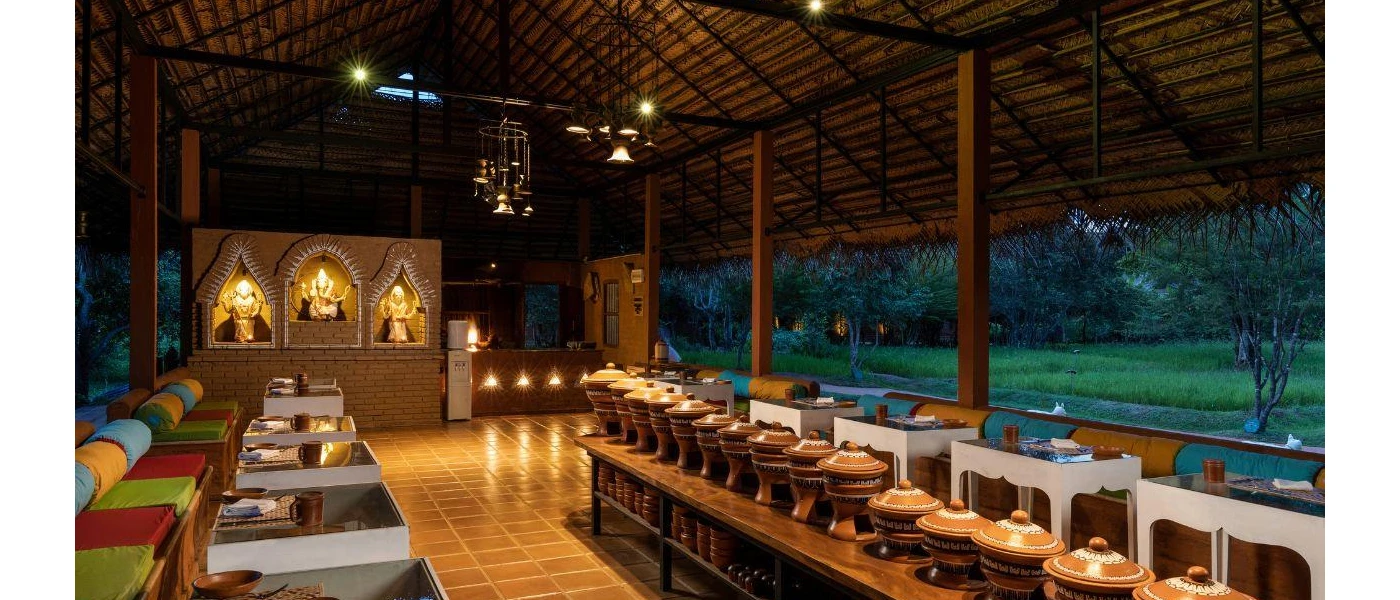 Inside a dining pavilion with white tables and colourful cushions around in a communal circle, with a table of pots at the centre