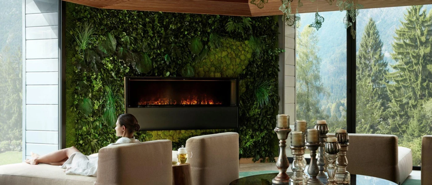 Woman relaxing in cushioned chairs in a robe, next to a fireplace adorned with greenery, and next to a table filled with candlesticks
