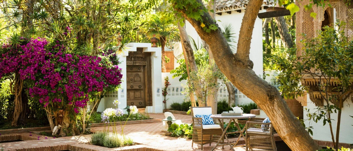 Whitewashed courtyard with a dark-wood door, purple bougainvillea, Arabic-style window shutters and a table and chairs  