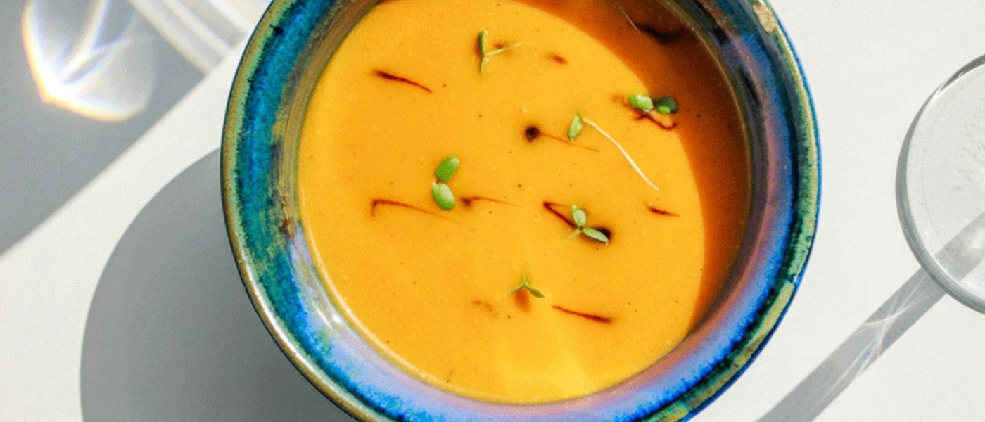Blue bowl with an orange-coloured soup with a herb garnish
