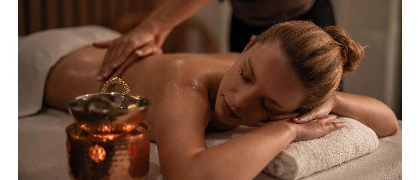 Woman lying with her head on a towel and her eyes closed, as a therapist massages her back