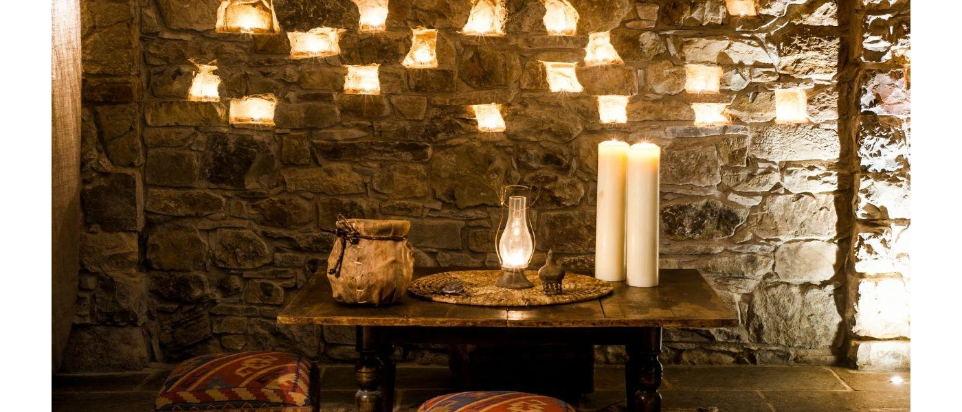 A stone wall and wooden table with candles places in the brickwork and on the table